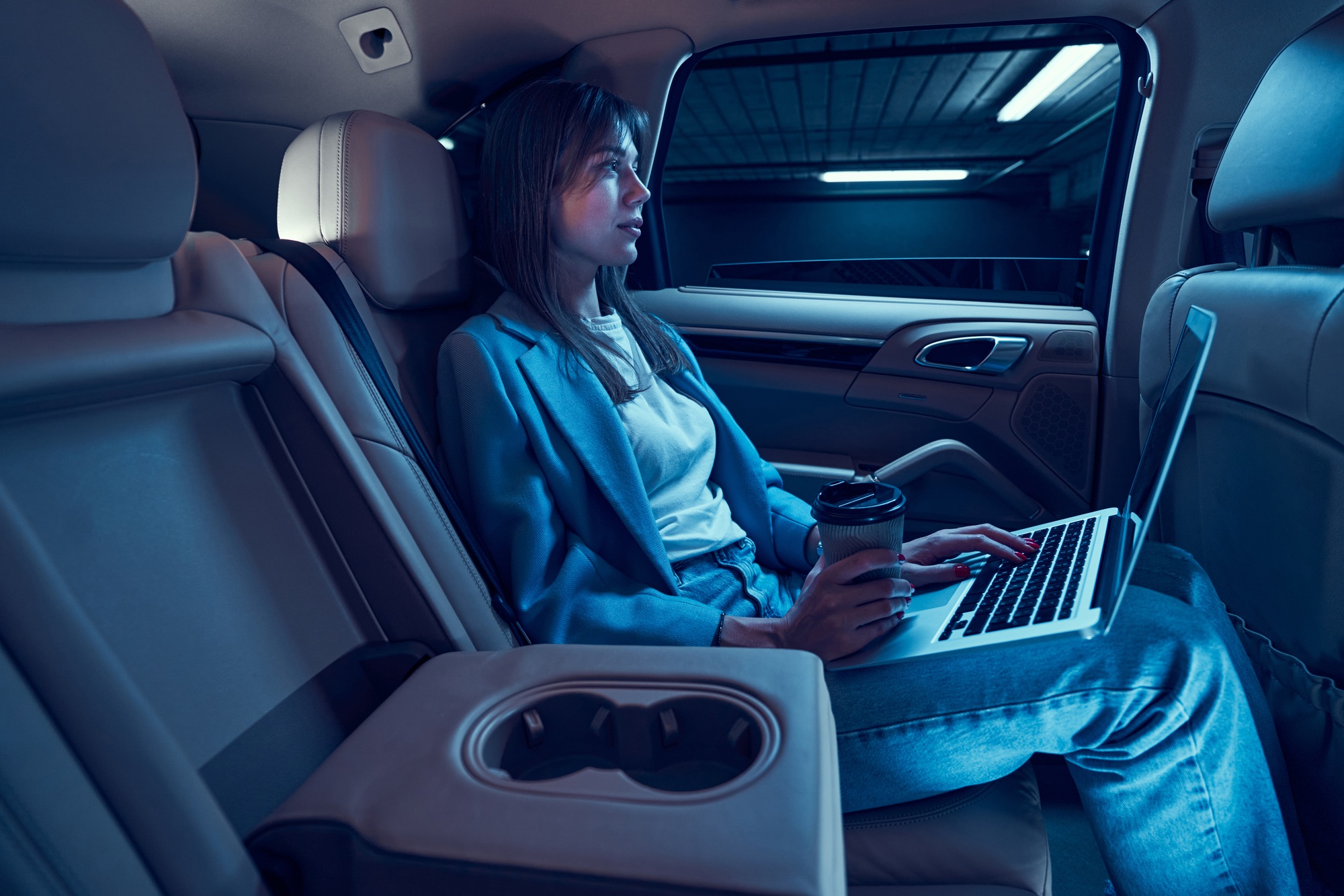 Woman drinking coffee and using laptop in car